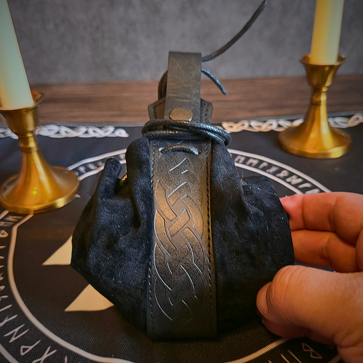 Hand holding a black leather-bound book with gold embossed text on a table with candles and a decorative cloth.