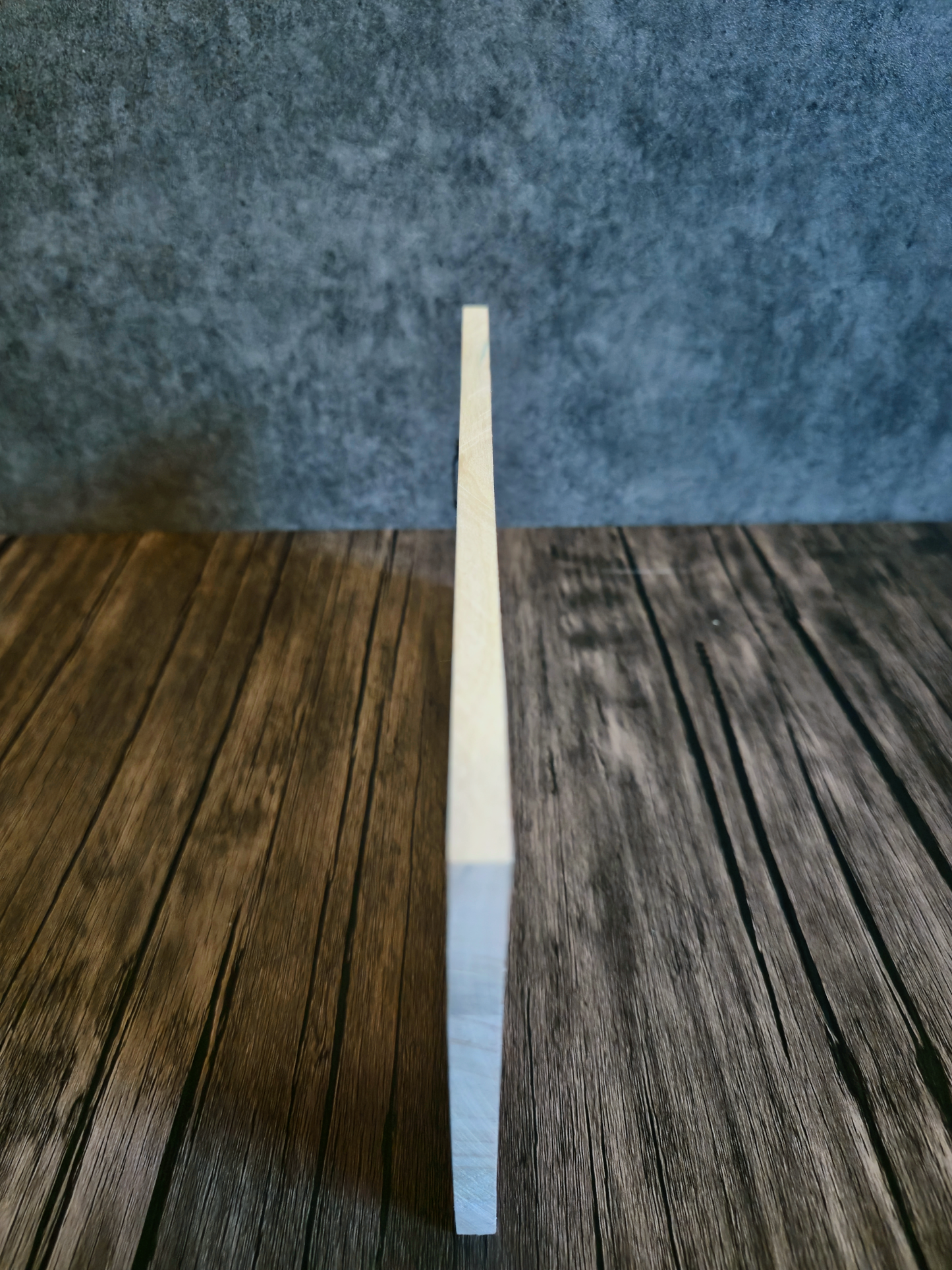 Side view of artwork showing thickness of wood on a wooden table with grey background.