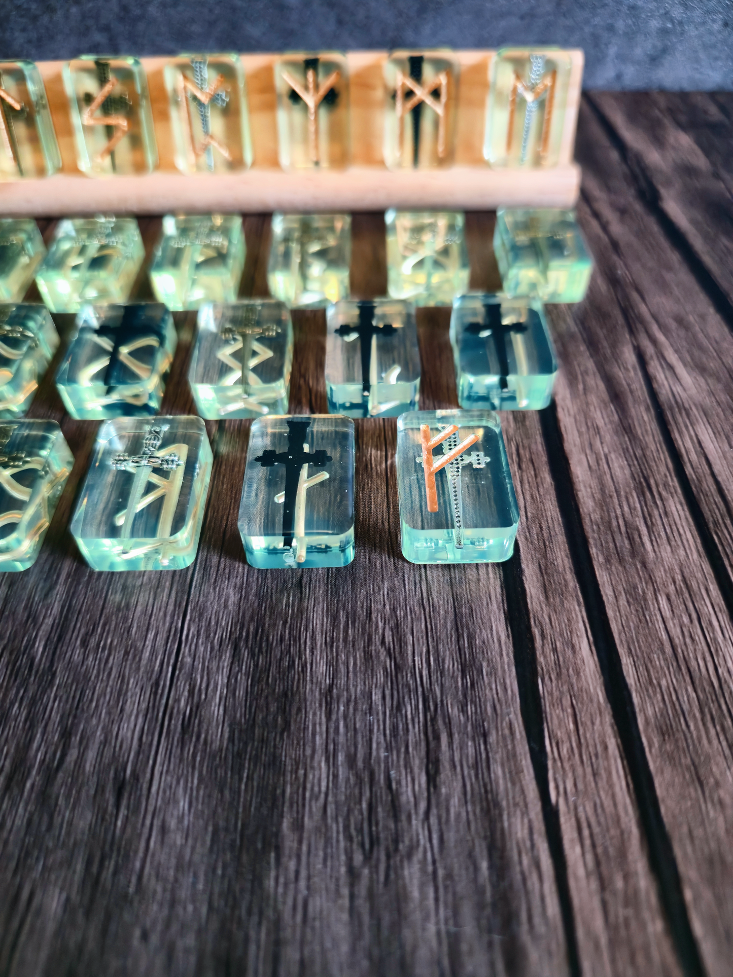 Up close view on runestones with greenish clear tint with golden Viking symbols on wooden table with birchwood stand in background.