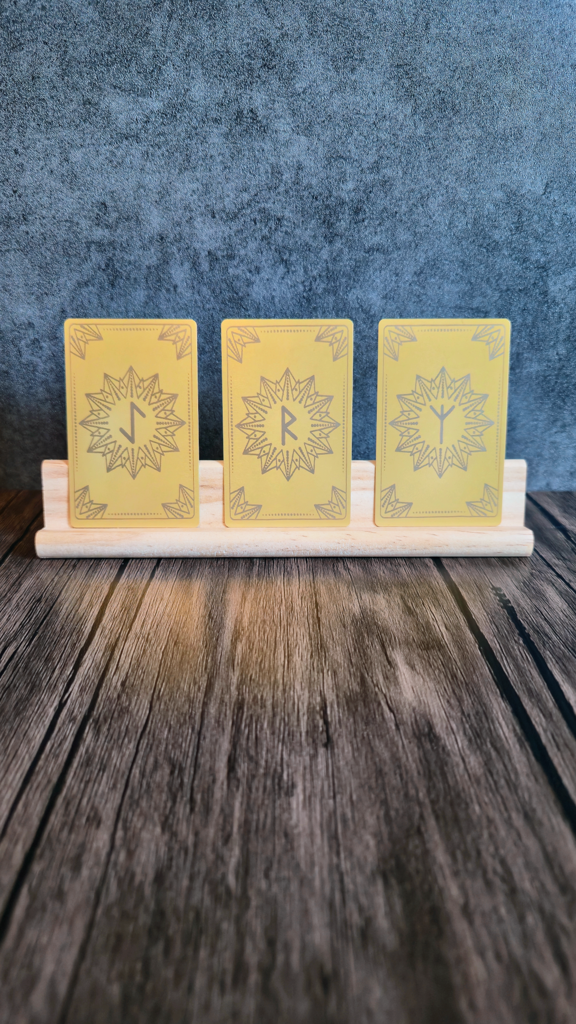 Three yellow cards with a symbol on a wooden stand against a blue textured background on a wooden table