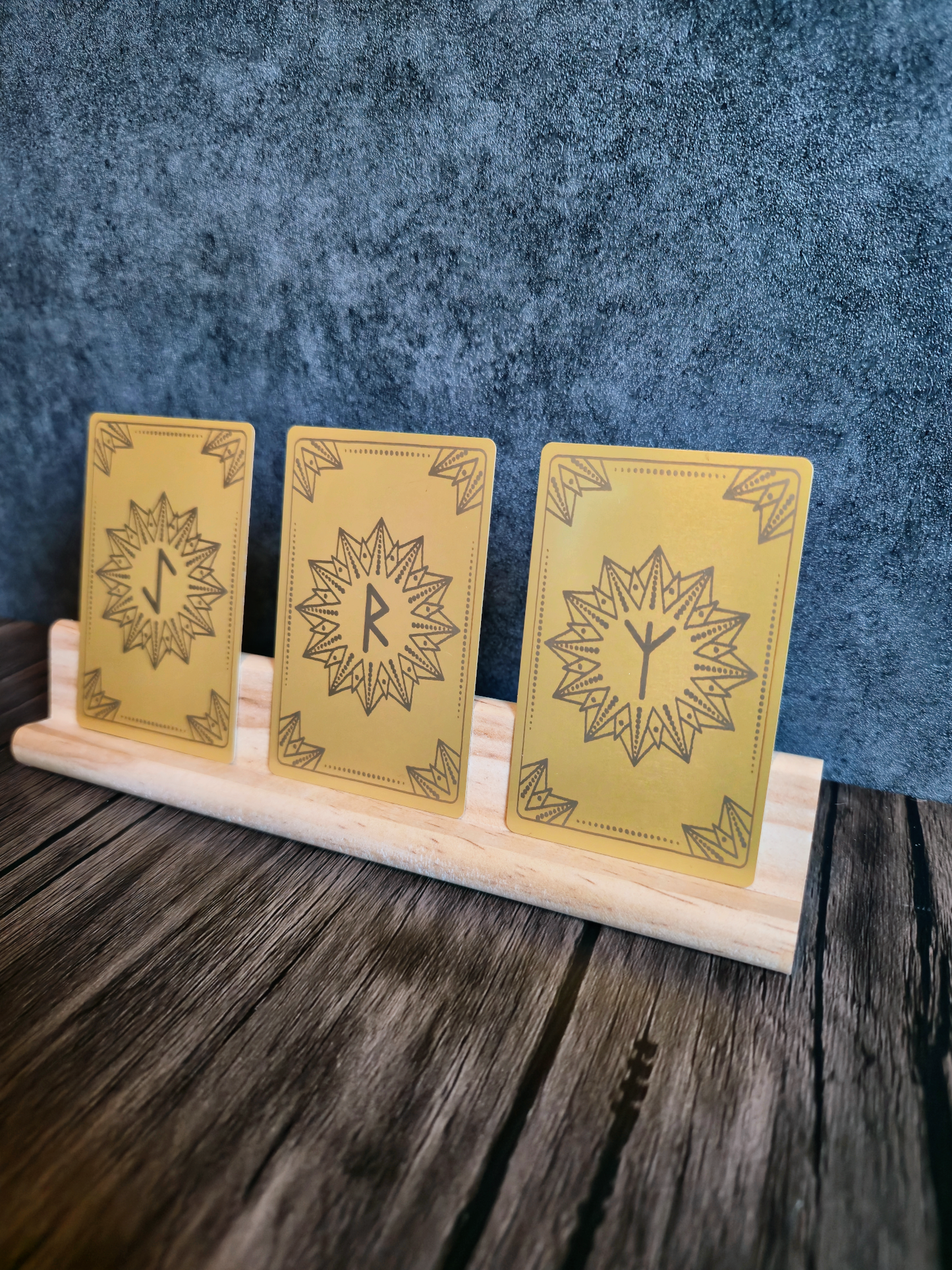 Three gold cards with star designs with Norse symbols on a wooden stand against a blue textured background