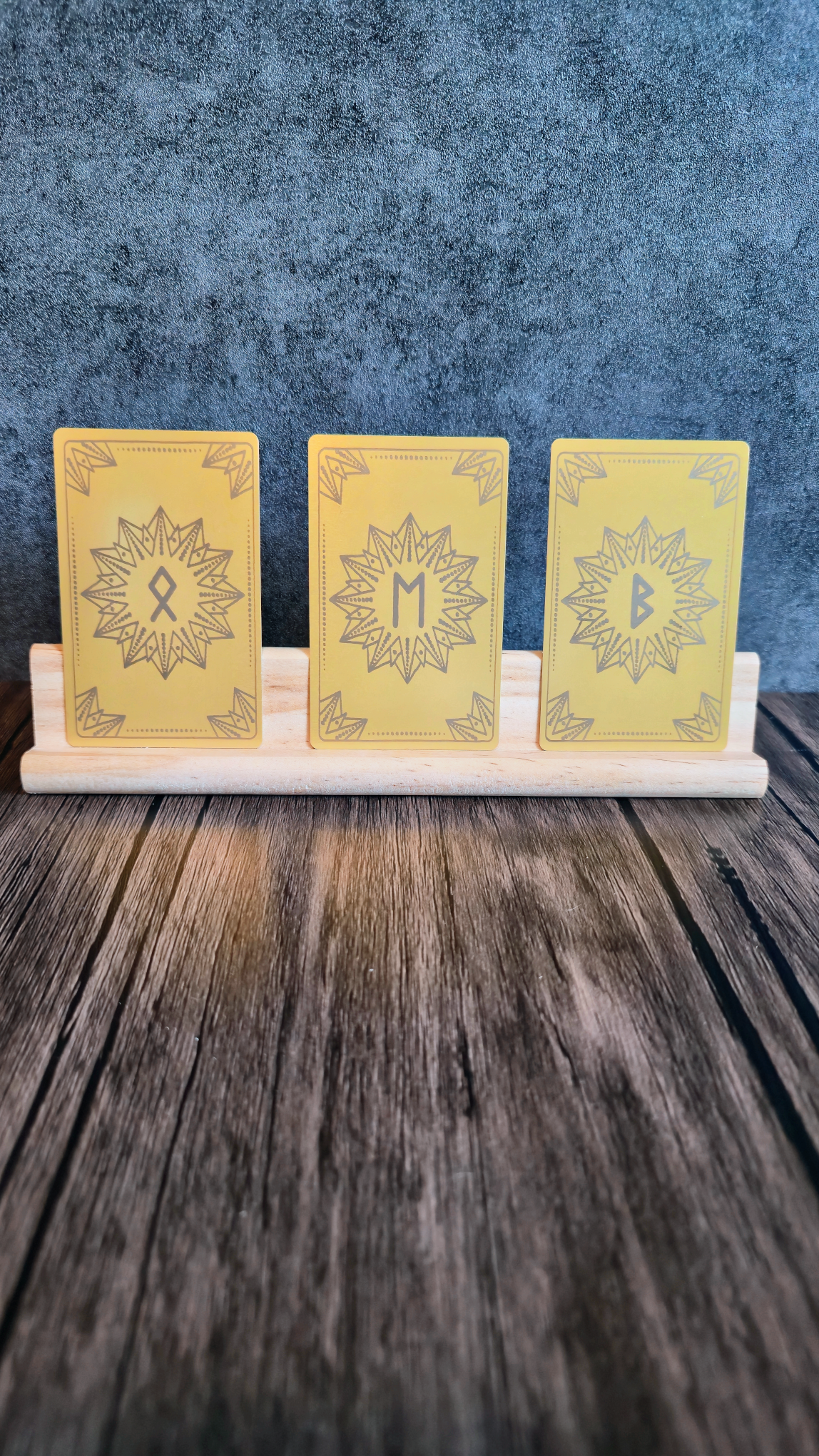 Three yellow cards with star designs and Runic symbols on a wooden stand against a blue textured background.