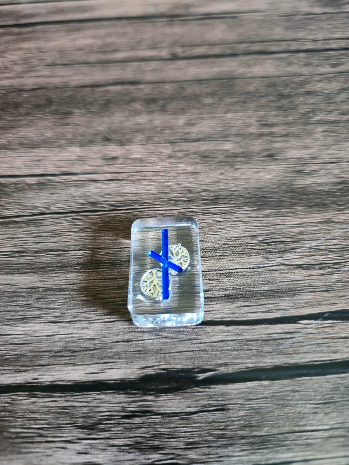 rune stone on wooden table with blue Norse symbol, golden beads of tree of life inside clear runestone