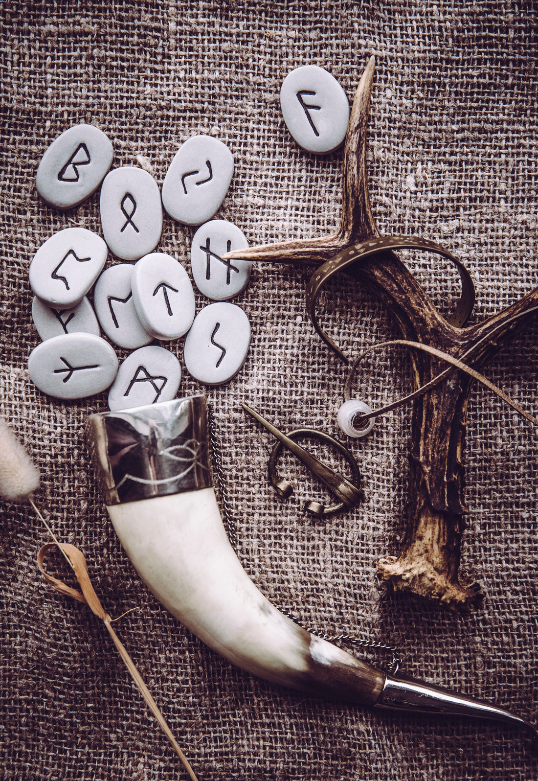 Runestones spread out before Viking Mead Horn cup with deer antler next to the stones, all laid on a burlap sack.