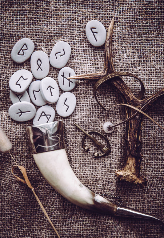 Runestones spread out before Viking Mead Horn cup with deer antler next to the stones, all laid on a burlap sack.