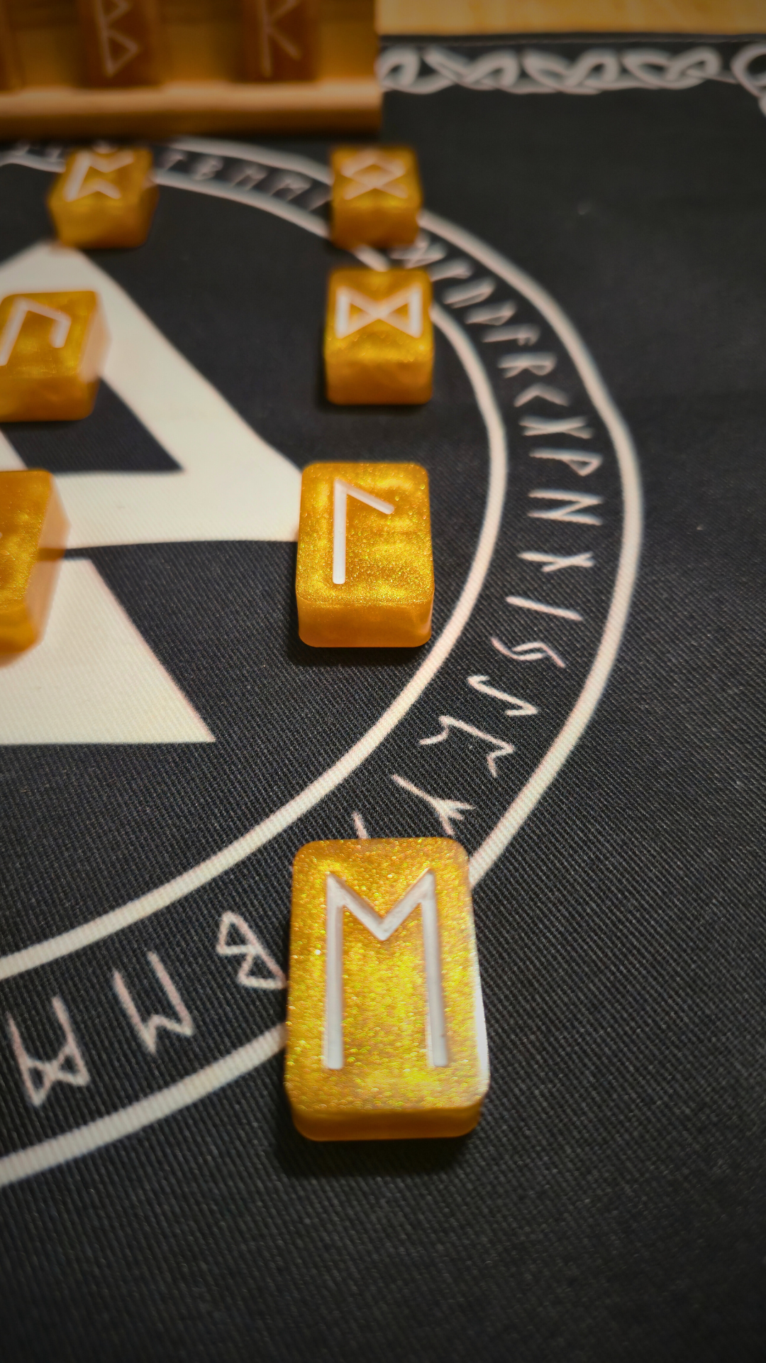 Close-up of Asgardian Gold Ingot Runestone Set: handcrafted gold resin ingots engraved with white Elder Futhark runes, arranged on a black rune cloth featuring a white Valknut symbol and circular runic border.