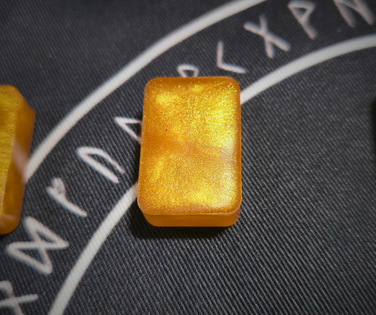 Glittering gold resin runestone ingot from the Asgardian Gold Ingot Runestone Set, showcasing a smooth metallic reverse side on a black cloth printed with white Elder Futhark runic circle.