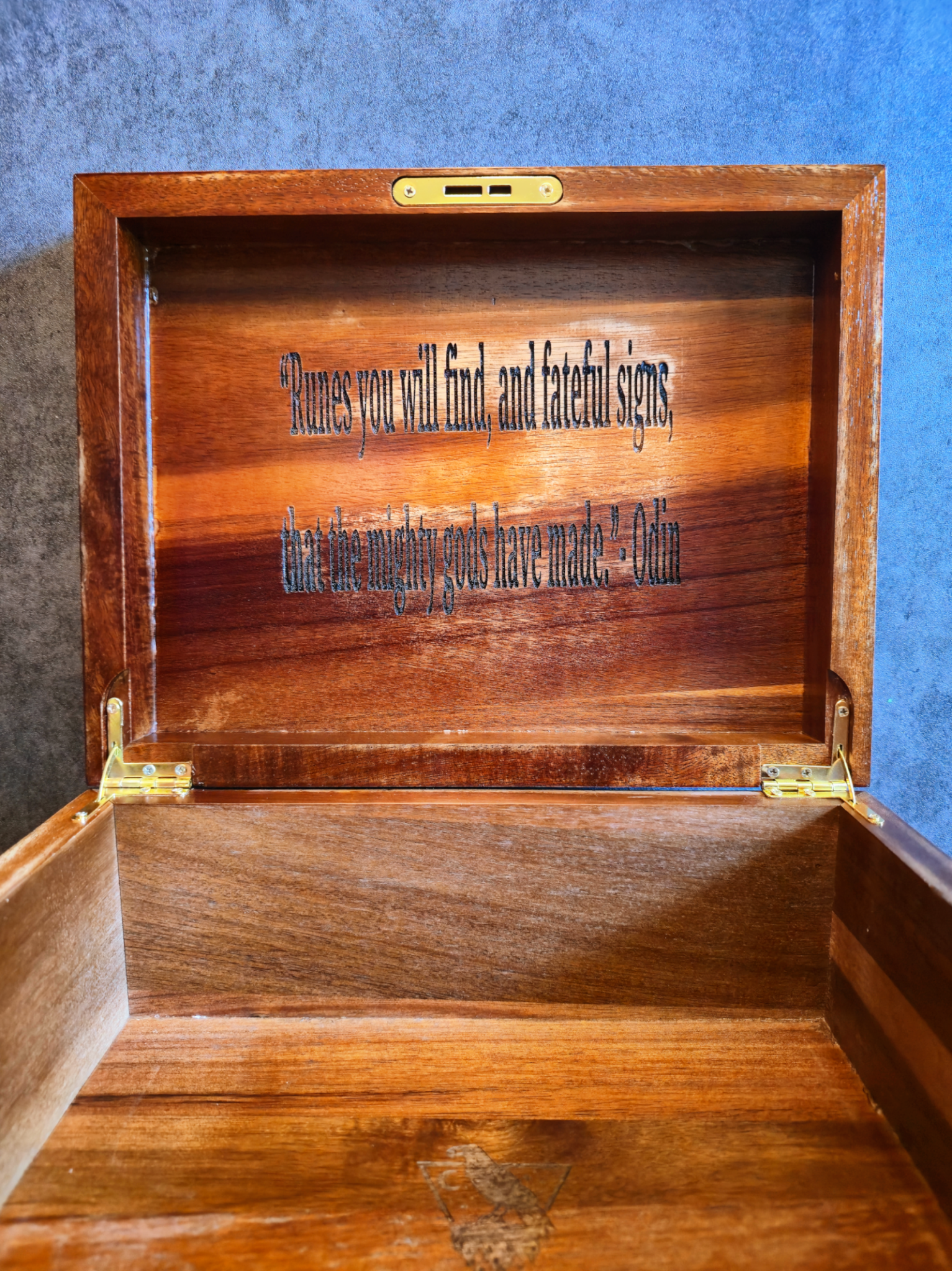 Interior of a handcrafted Norse Runestones wooden chest showing the inside of the lid engraved with Odin’s quote ‘Runes you will find, and fateful signs, that the mighty gods have made,’ and the base featuring a subtle raven emblem on polished mahogany.