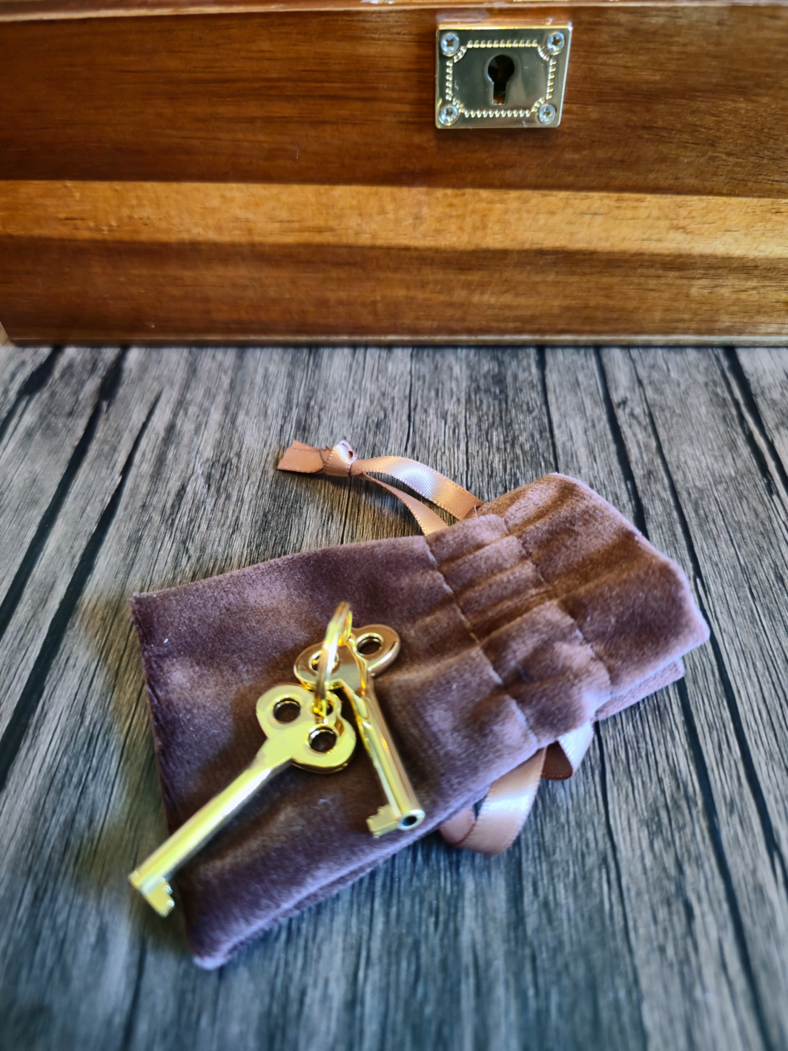 A soft velvet pouch lying open on a wooden surface, spilling two small brass keys beside the keyhole of a handcrafted wooden box.