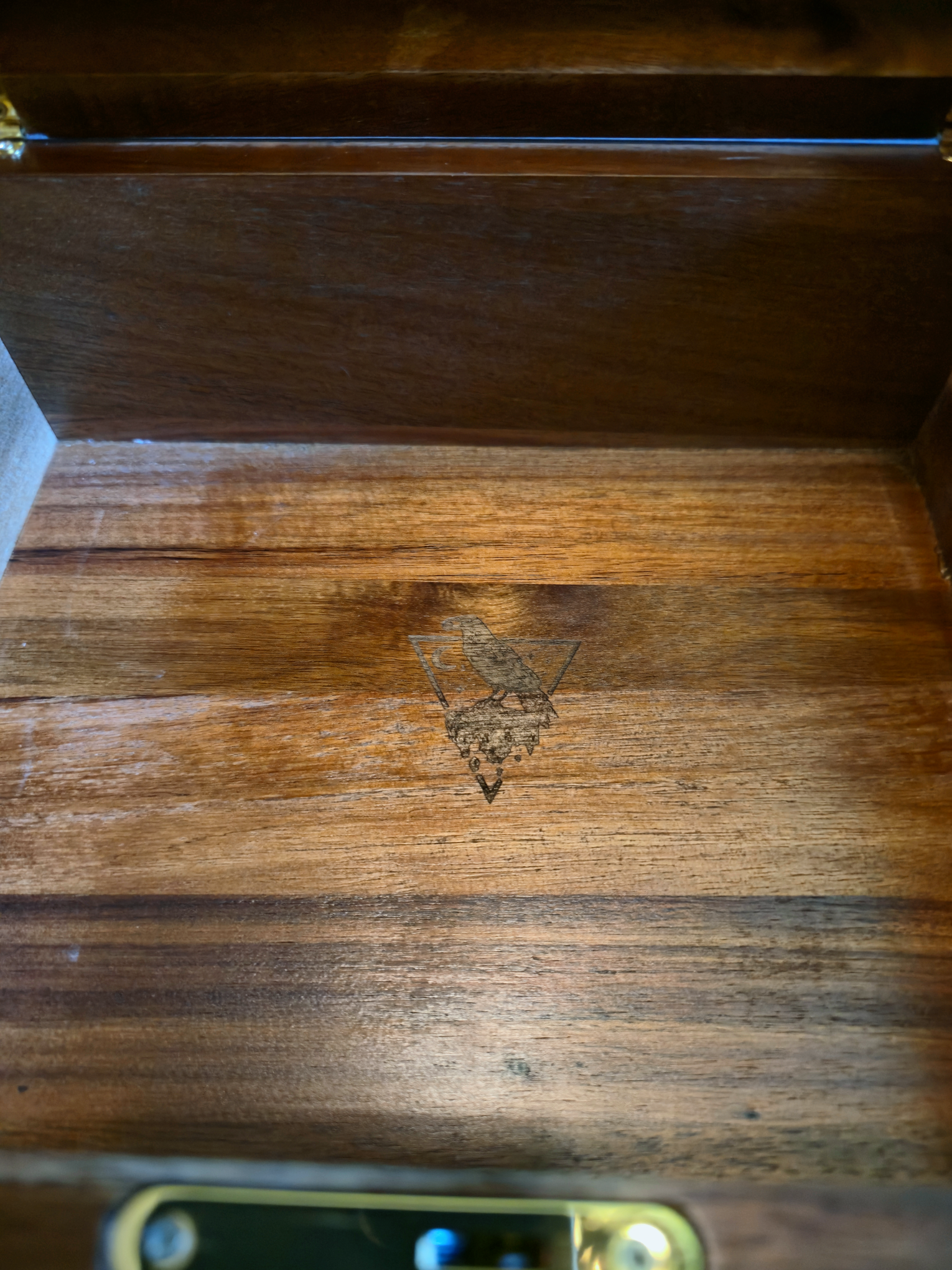 Close-up of the empty interior of a handcrafted wooden box, revealing a subtle raven emblem laser-etched into the polished mahogany base.