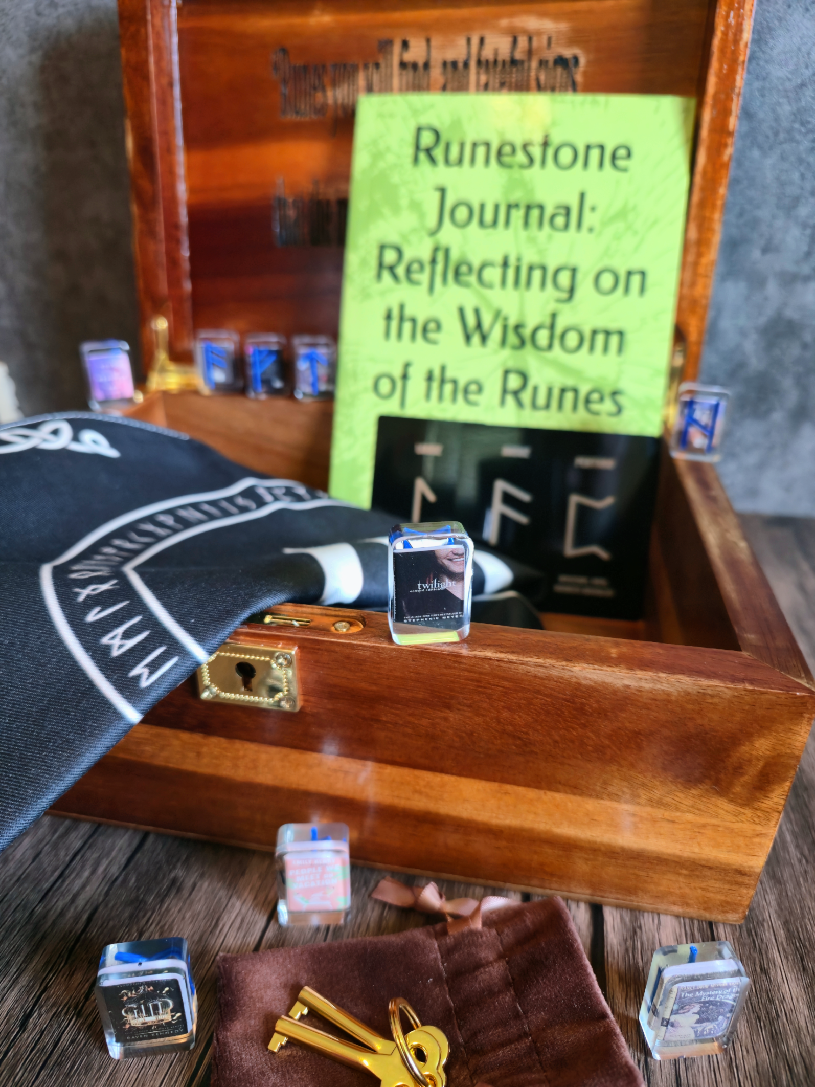Wooden box with mystical items including a Runestone Journal and key, on a wooden surface.