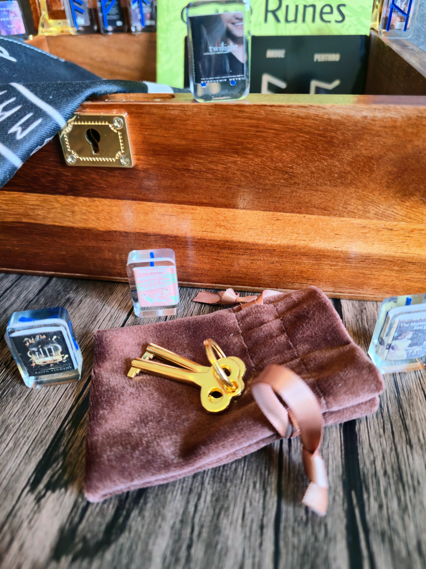 Wooden box with gold keys on a plush pillow, surrounded by various items on a wooden surface.