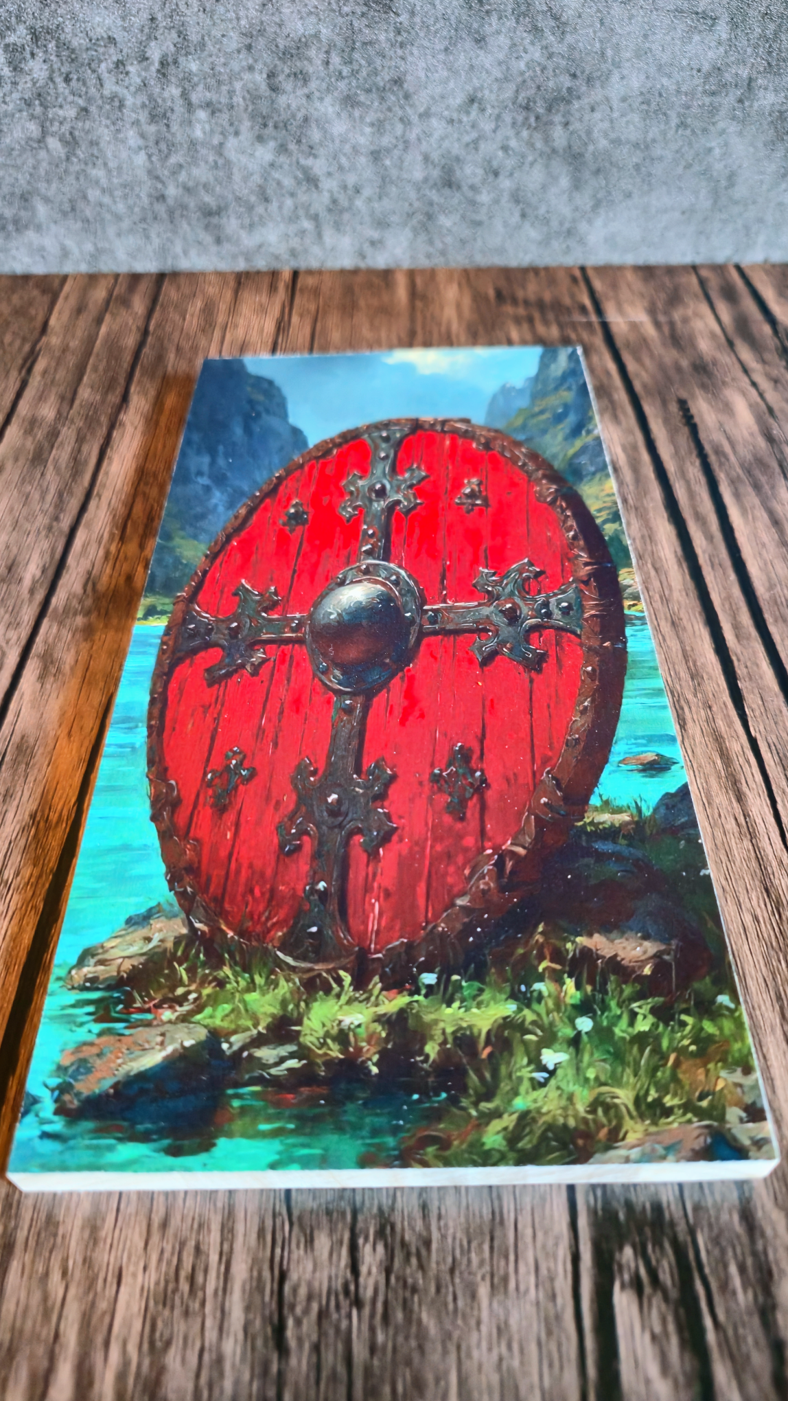 Artwork of  red Viking shield with mountain background on wood.
